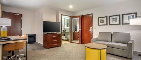 A hotel room with a desk, chair, sofa, television, and a small yellow table.