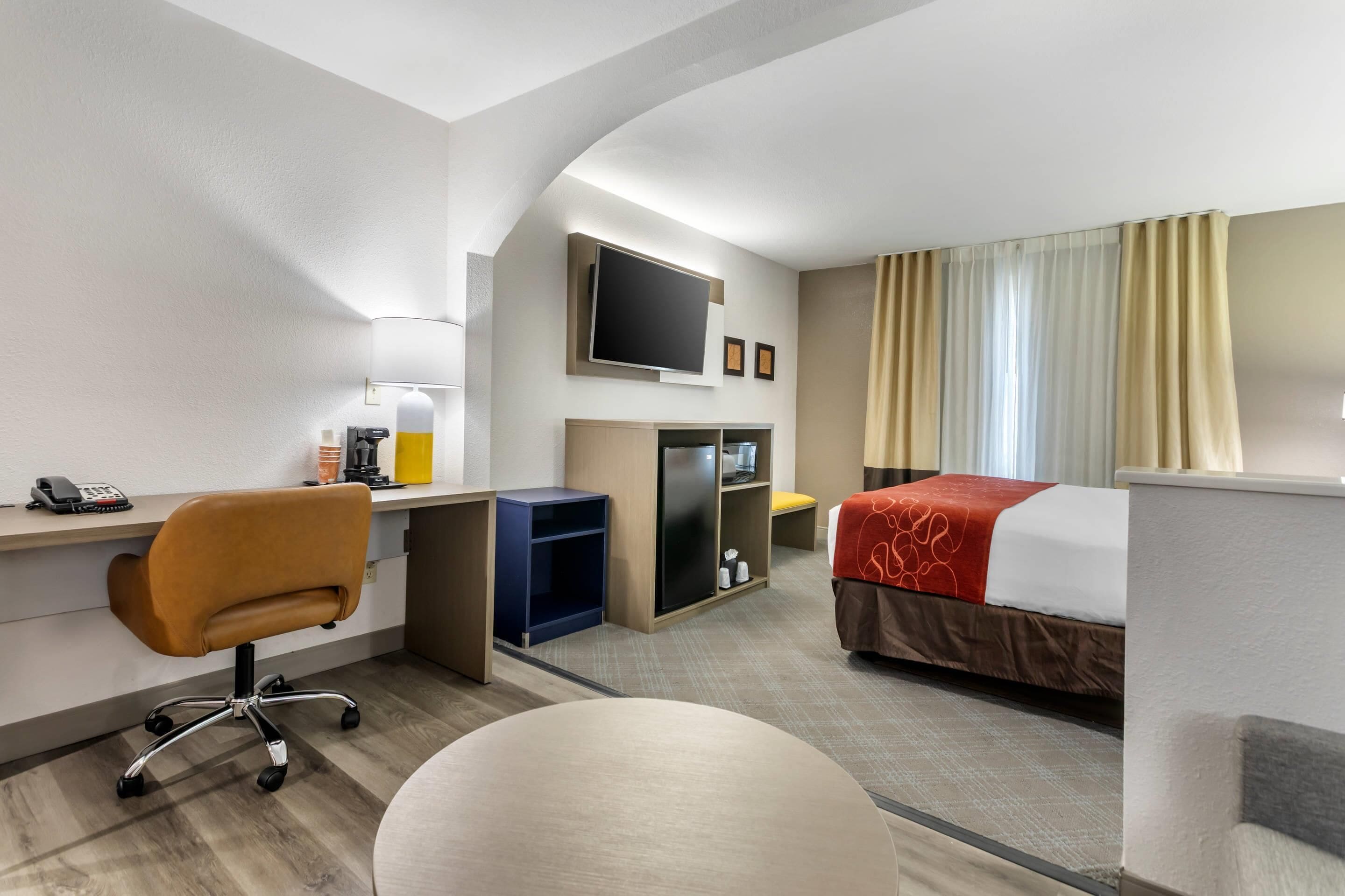 Une chambre d’hôtel équipée d’un bureau, d’une chaise, d’un lit, d’une télévision et d’un petit coin salon.