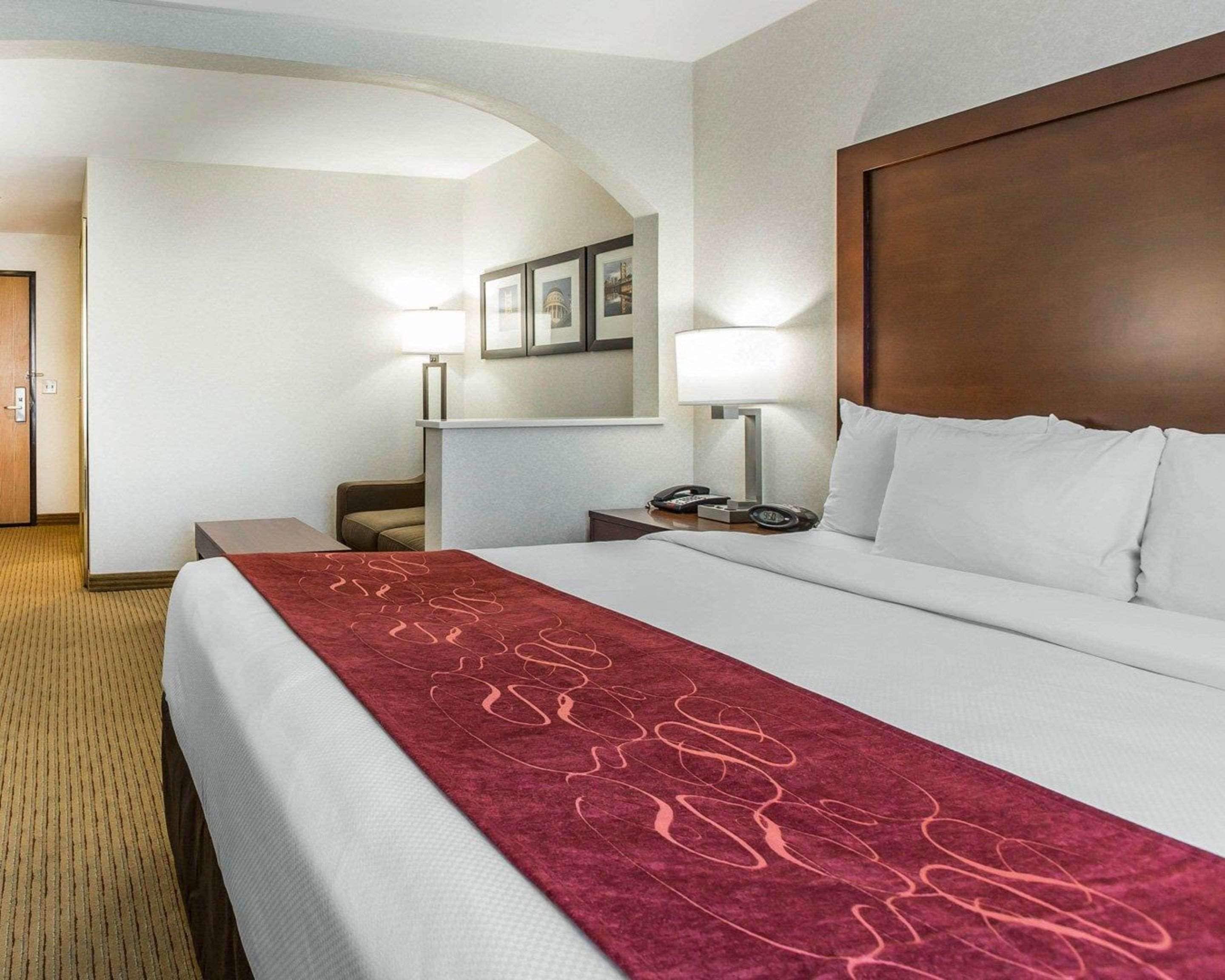 A hotel room with a large bed, a desk, a chair, a nightstand, a lamp, and a wall-mounted TV.