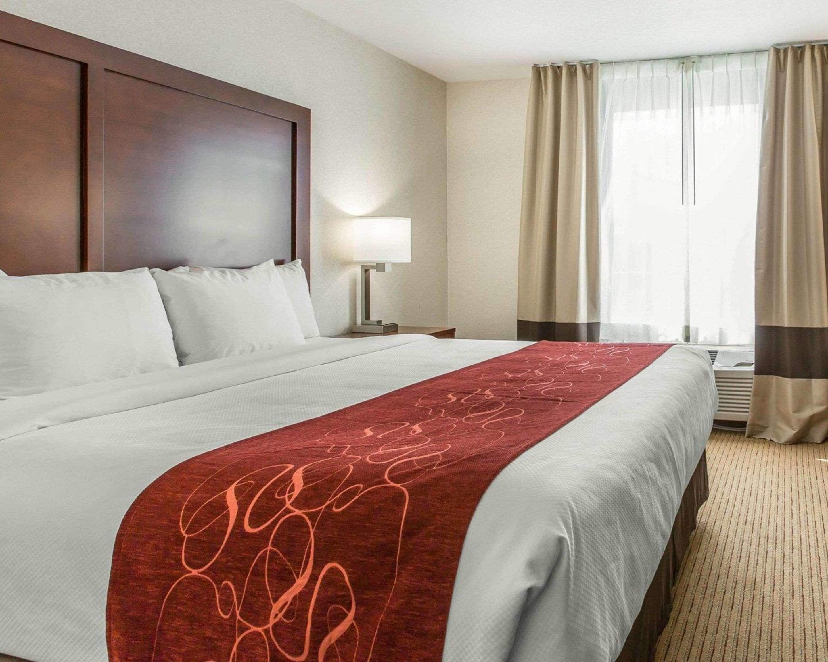 A hotel room with a large bed, a wooden headboard, a bedside table with a lamp, and a window with curtains.