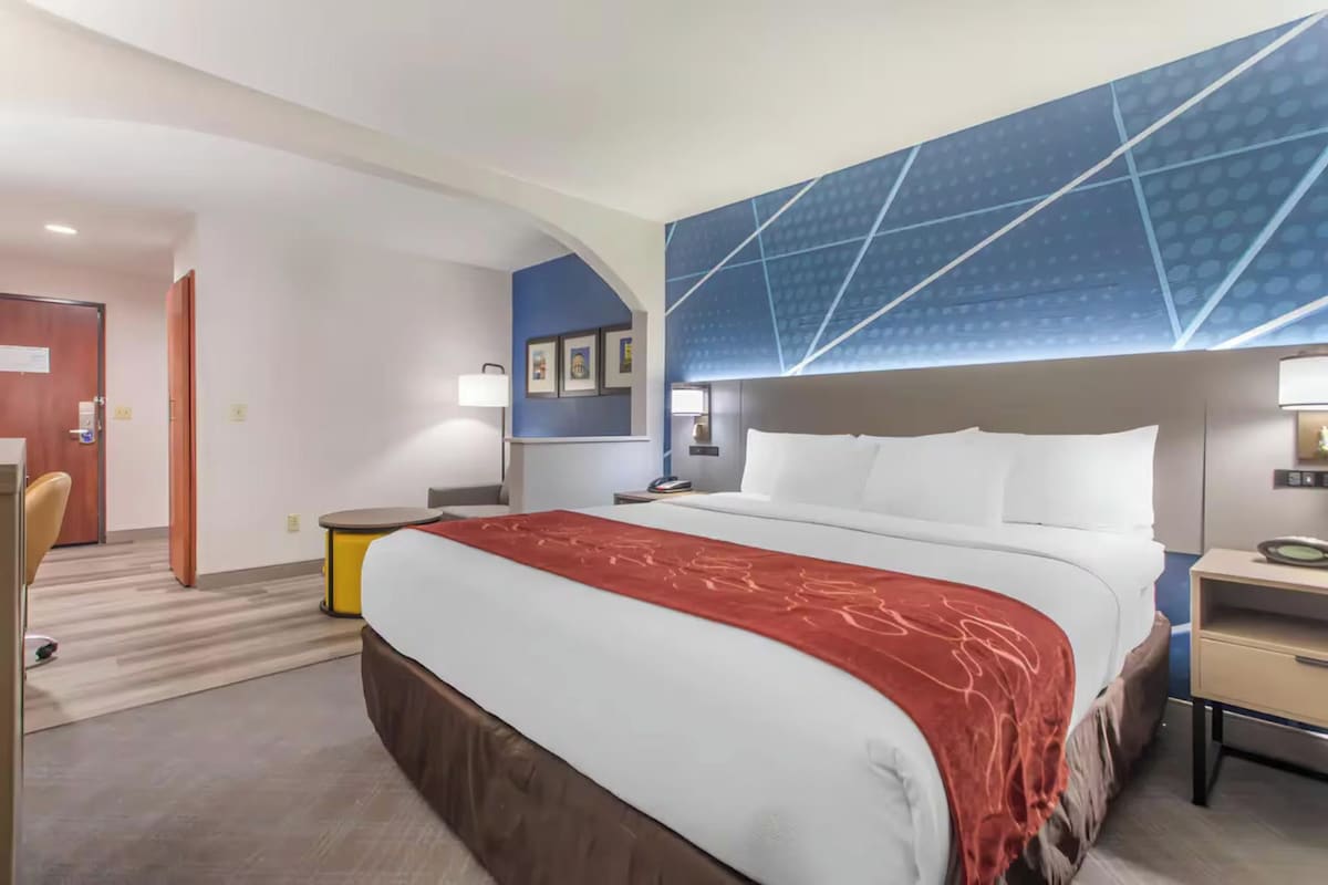 A hotel room with a large bed, a desk, a chair, and a blue accent wall.