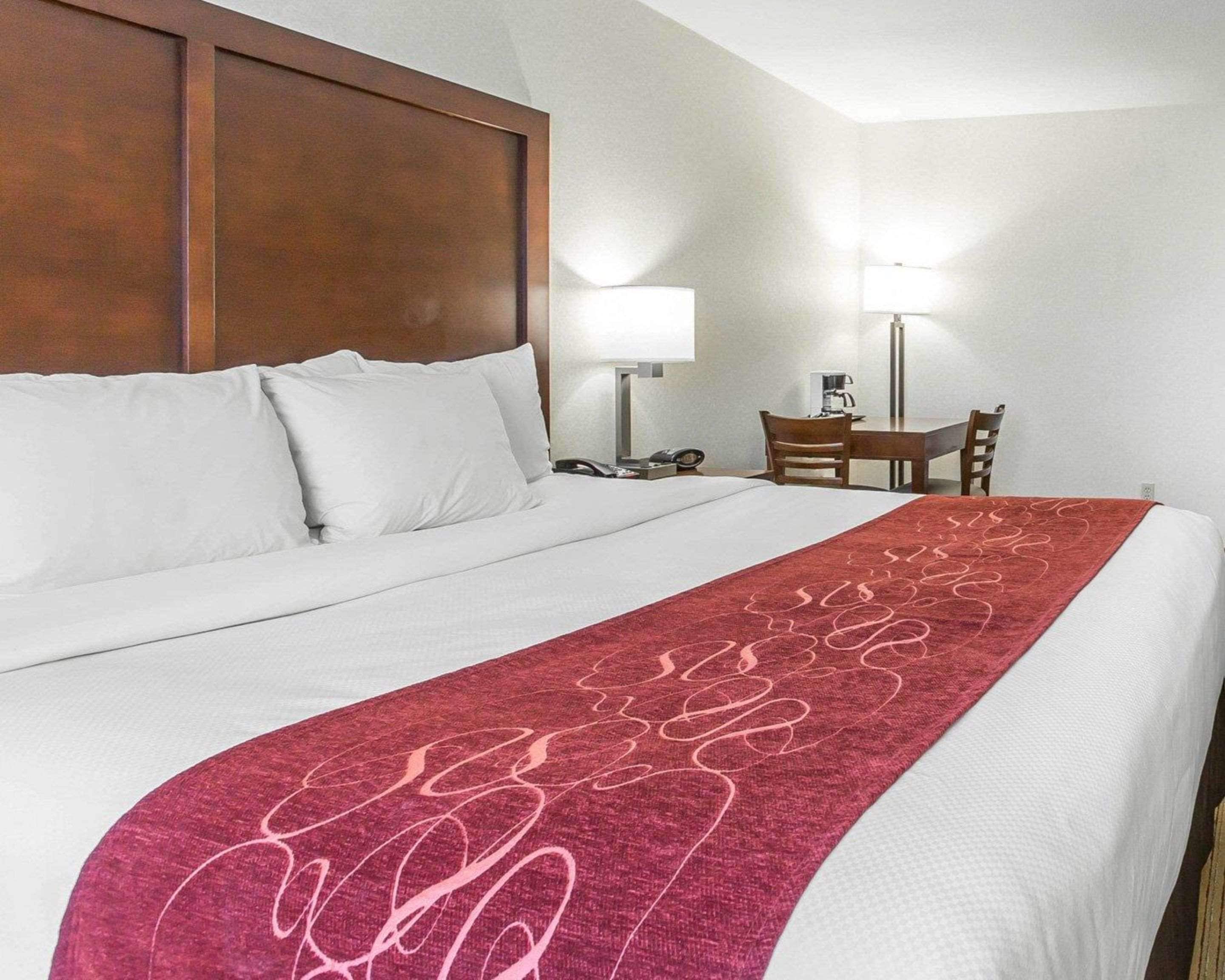 A hotel room with a large bed, a wooden headboard, a desk with a chair, and two bedside lamps.