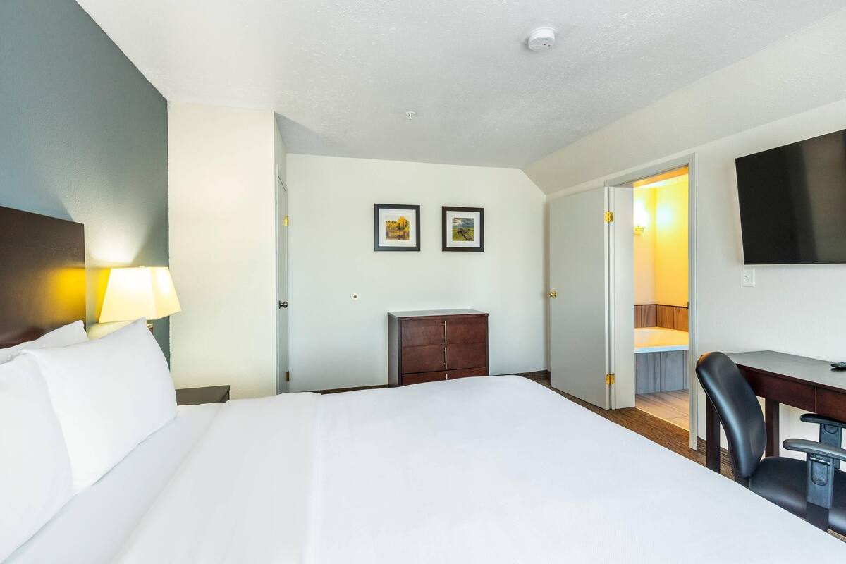 A hotel room with a large bed, a desk, a chair, a wardrobe, and a TV mounted on the wall.