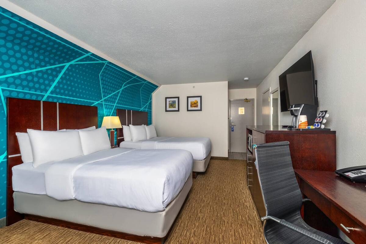A hotel room with two beds, a desk, a chair, a TV, and a coffee machine.