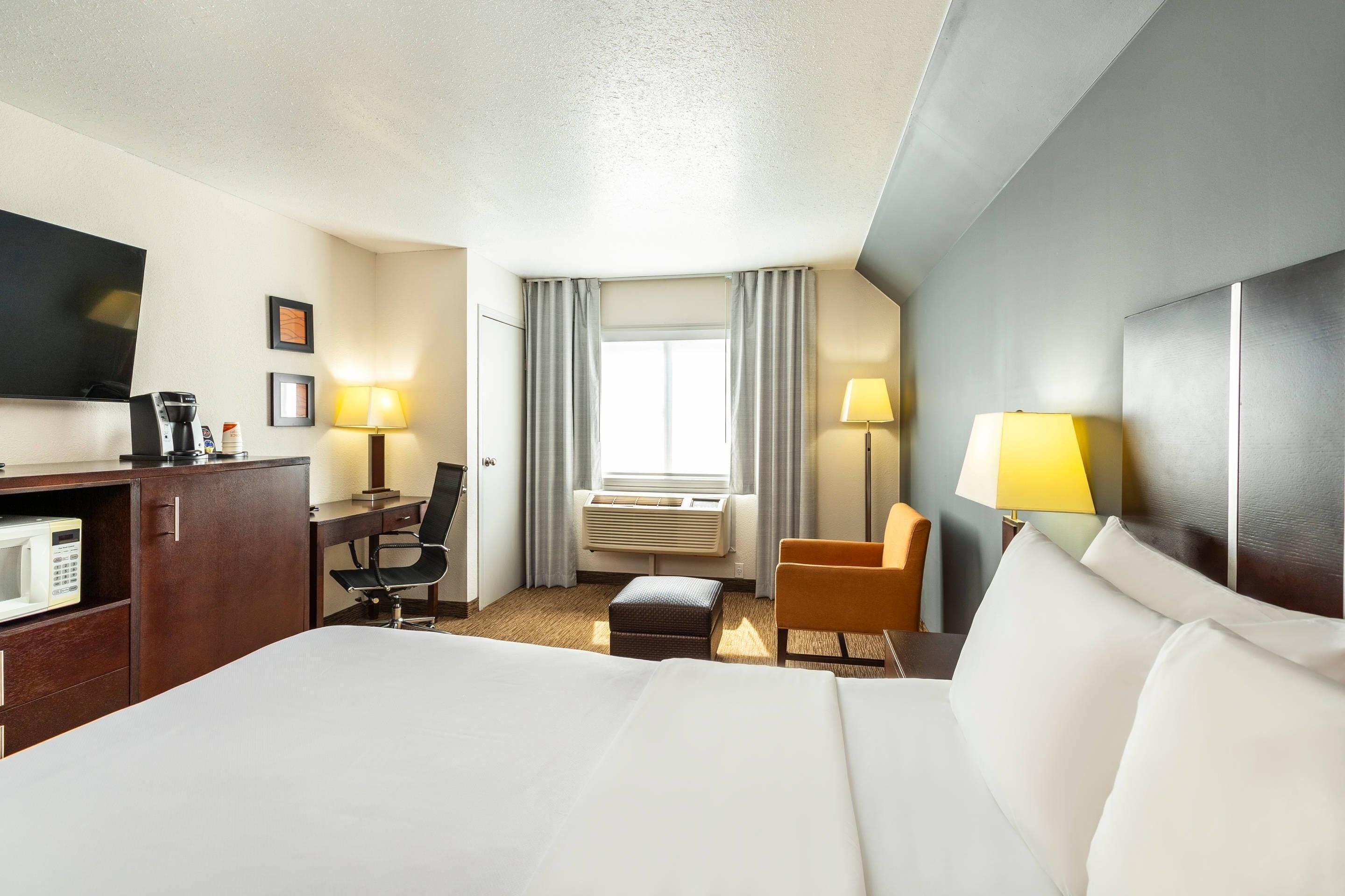 A hotel room with a large bed, a desk with a computer, a chair, a TV, and a window with curtains.