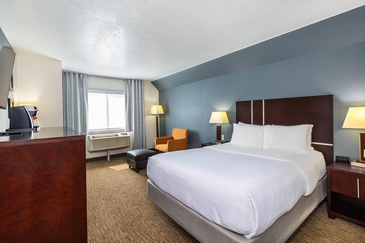A hotel room with a large bed, a desk, a chair, and a nightstand.