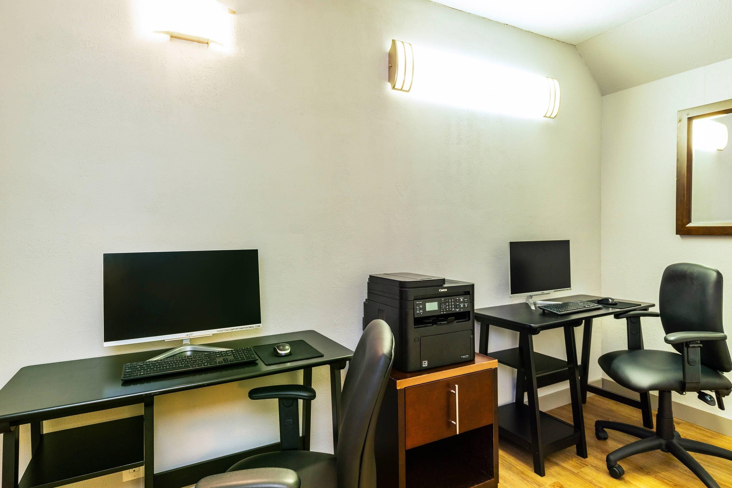 A modern office space with two desks, one with a desktop computer and keyboard, and another with a printer and laptop.