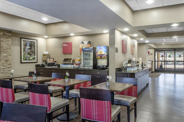 A restaurant with multiple tables and chairs, a beverage dispenser, and a counter with food items.