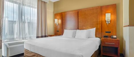 A hotel room with a large bed, bedside lamps, a heater, and a window with curtains.