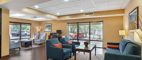 A hotel lobby with seating, a reception desk, large windows, and a view of the outside.