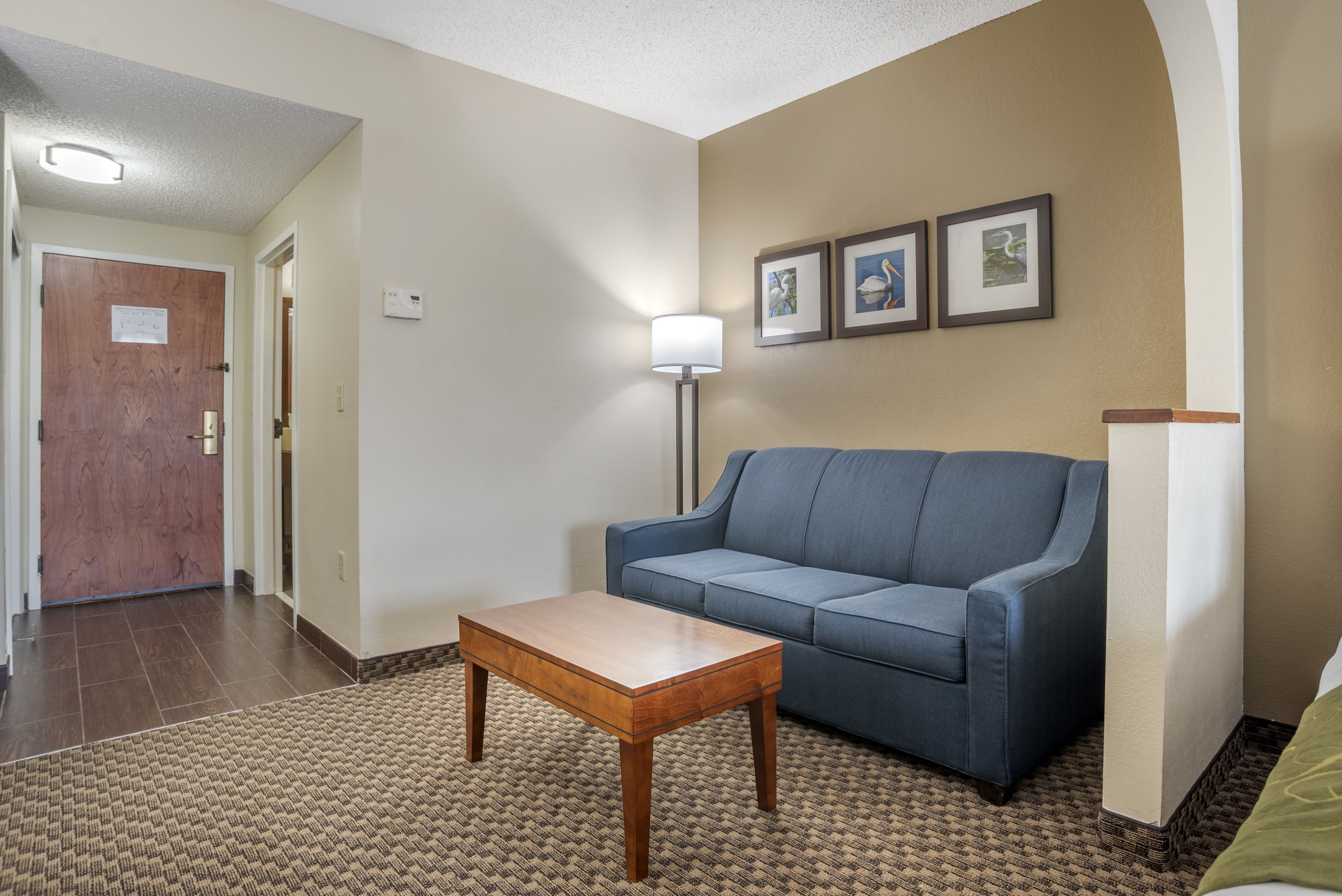 A room with a wooden table, a blue sofa, and a lamp. There are framed pictures on the wall.