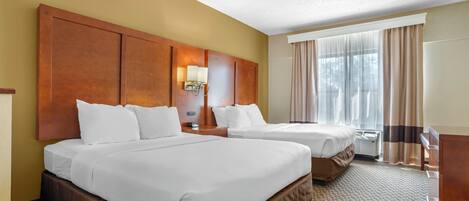 A hotel room with two beds, a wooden headboard, a nightstand with a lamp, and a large window with curtains.