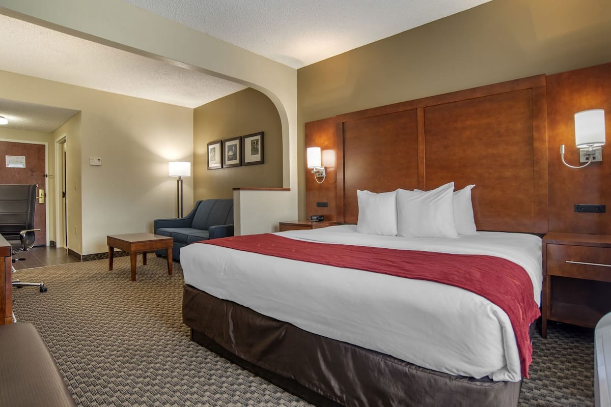 A hotel room with a large bed, a desk, a chair, and a lamp.