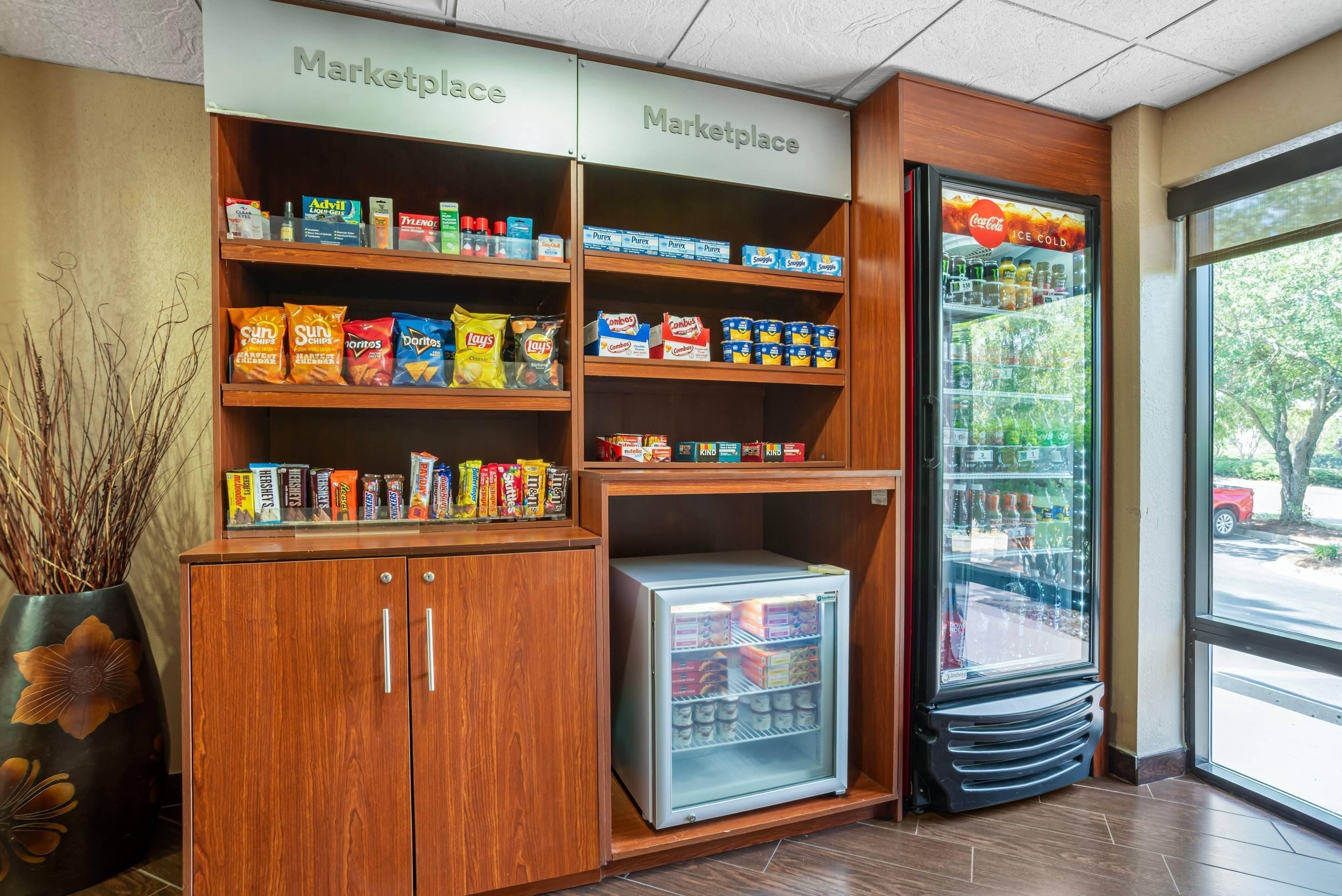 Una zona de kitchenette con un refrigerador, estantes llenos de aperitivos y una máquina expendedora.