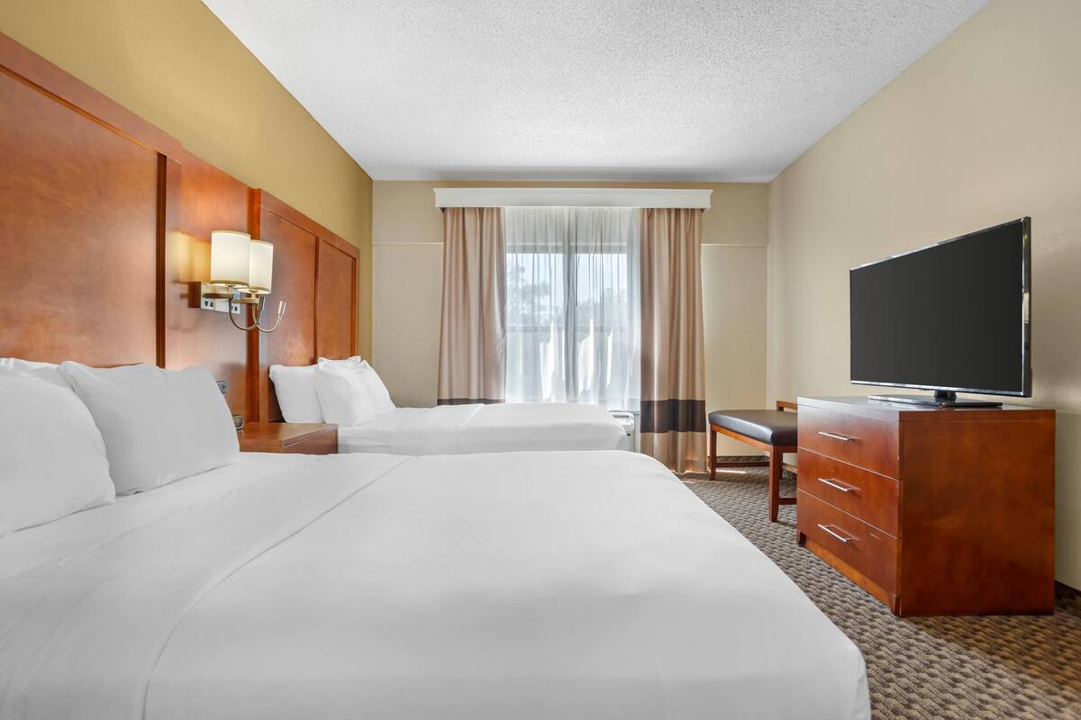 A hotel room with two beds, a TV, a desk, and a chair.