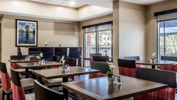 Un restaurant avec des banquettes et des tables, dont certaines sont décorées de fleurs. Il y a une grande fenêtre et un tableau au mur.