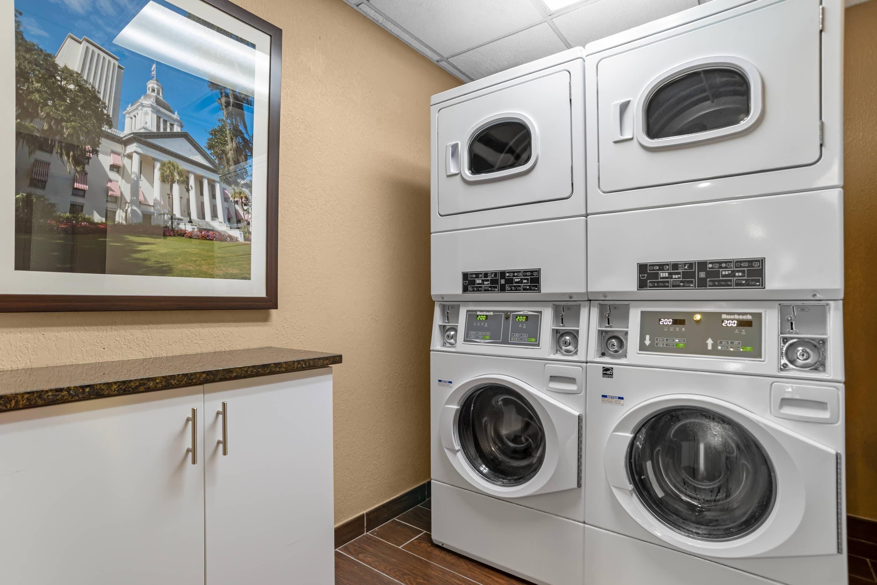 A laundry area with stacked washers and dryers, a framed picture of a building, and a white cabinet.