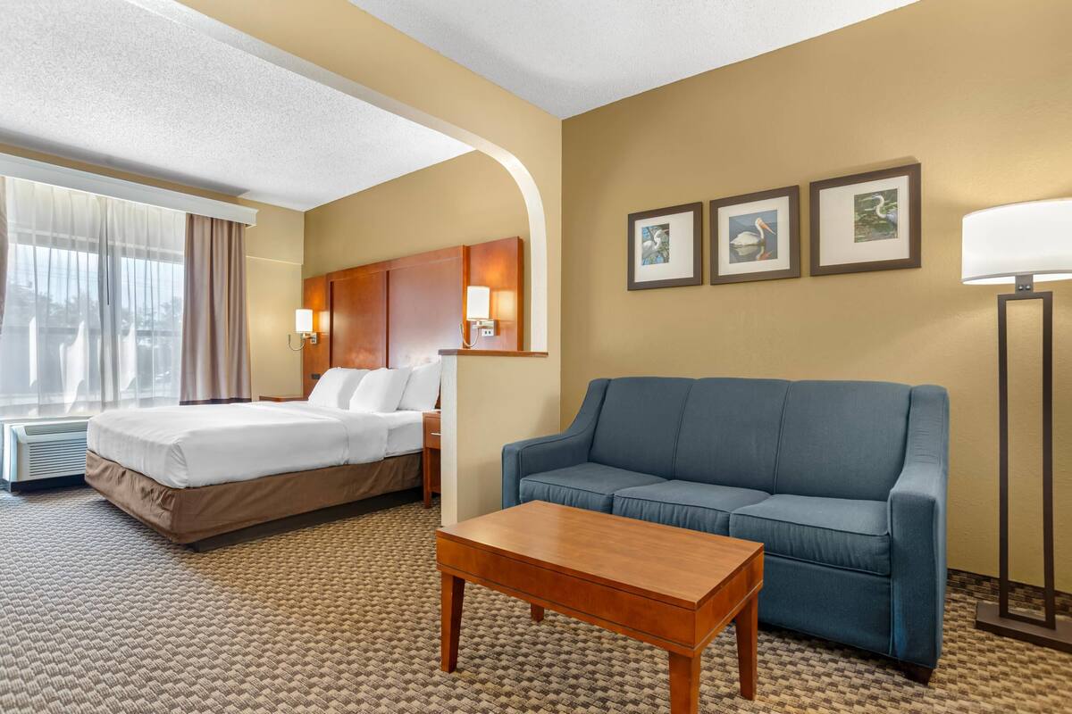 A hotel room with a bed, a sofa, a coffee table, and a lamp.