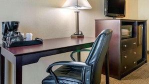 A hotel room with a desk, a chair, a coffee maker, a television, and a minibar.