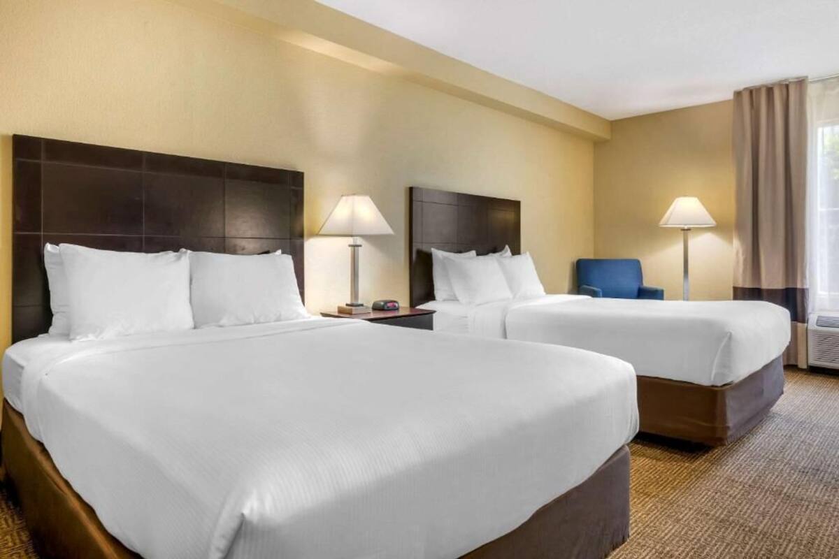 A hotel room with two beds, a nightstand, a lamp, a chair, and a window with curtains.
