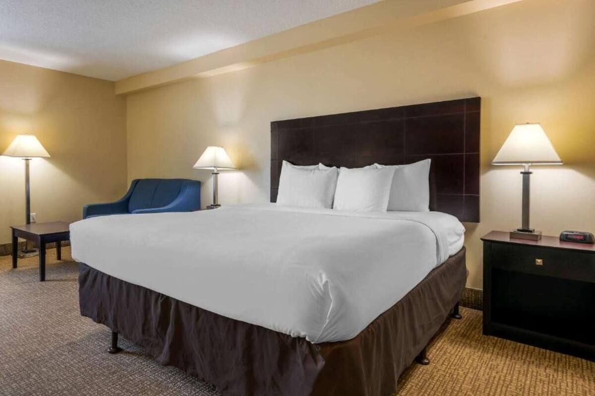 A hotel room with a large bed, two bedside tables, a chair, and two lamps.