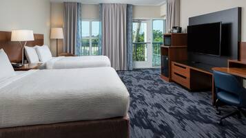 A hotel room with two beds, a TV, a desk, and a view of the outdoors.