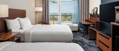 A hotel room with two beds, a desk, a chair, a television, and a balcony with a view.