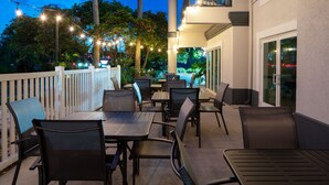 An outdoor patio area with tables and chairs, string lights, and a view of the surrounding greenery.