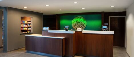A reception area with two wooden reception desks, a green wall with a spherical design, and a snack shelf to the left.