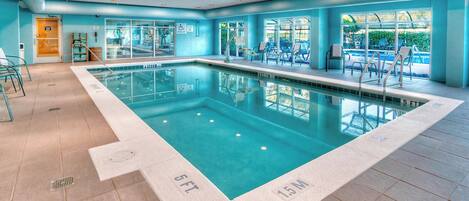 Una piscina con agua cristalina, rodeada de paredes azules y un suelo de baldosas. Hay sillas de descanso y un ventanal con vistas a la vegetación.