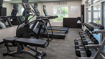 Une salle de sport équipée de tapis de course, d’un appareil elliptique, d’un banc de musculation et d’haltères.