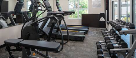 A fitness center with treadmills, an elliptical, a bench, and dumbbells.