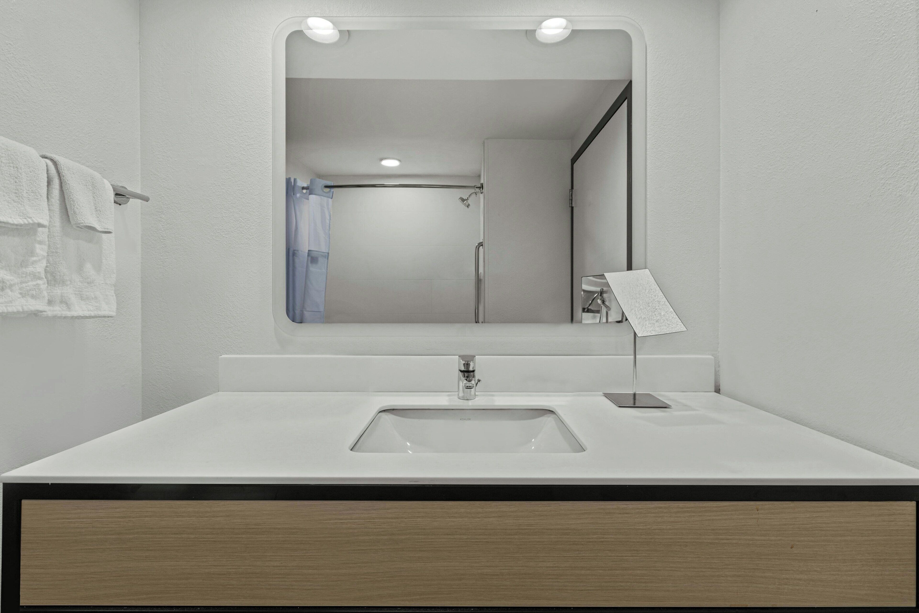 A modern bathroom with a white sink, a mirror, and a shower visible in the background.