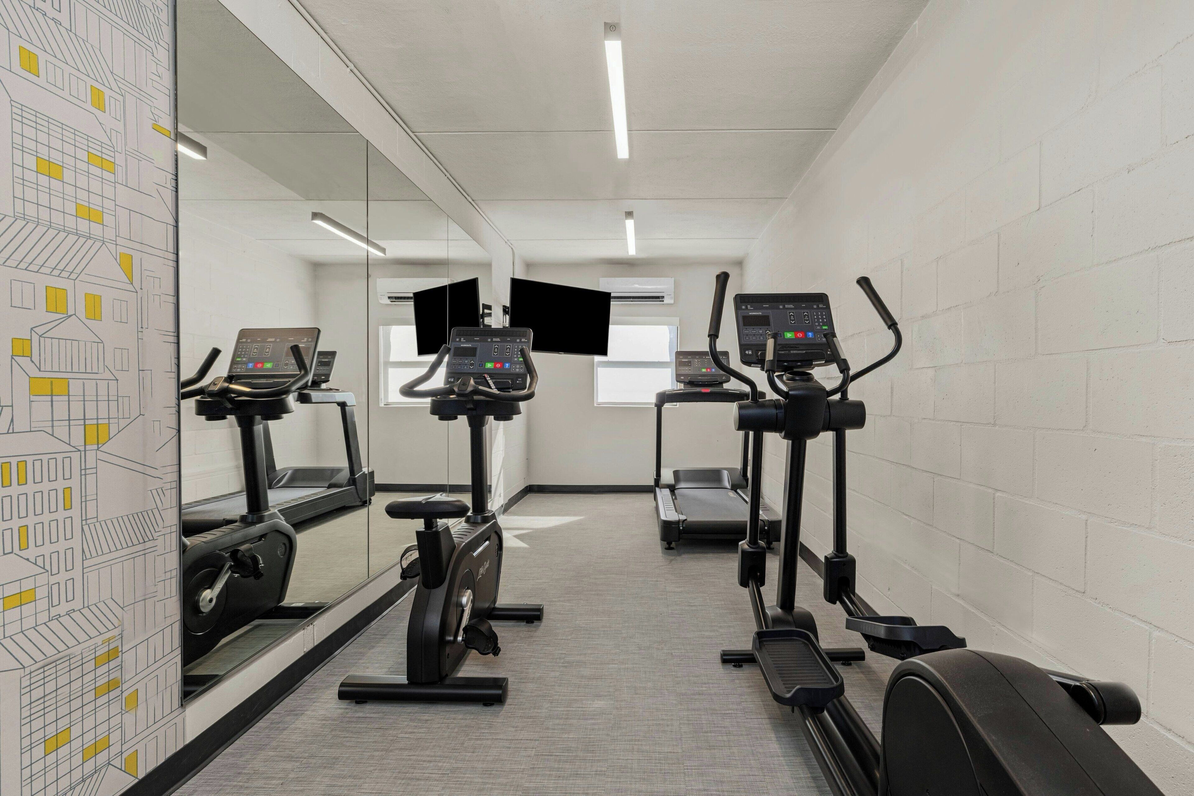 A gym with treadmills, stationary bikes, and a mirrored wall.