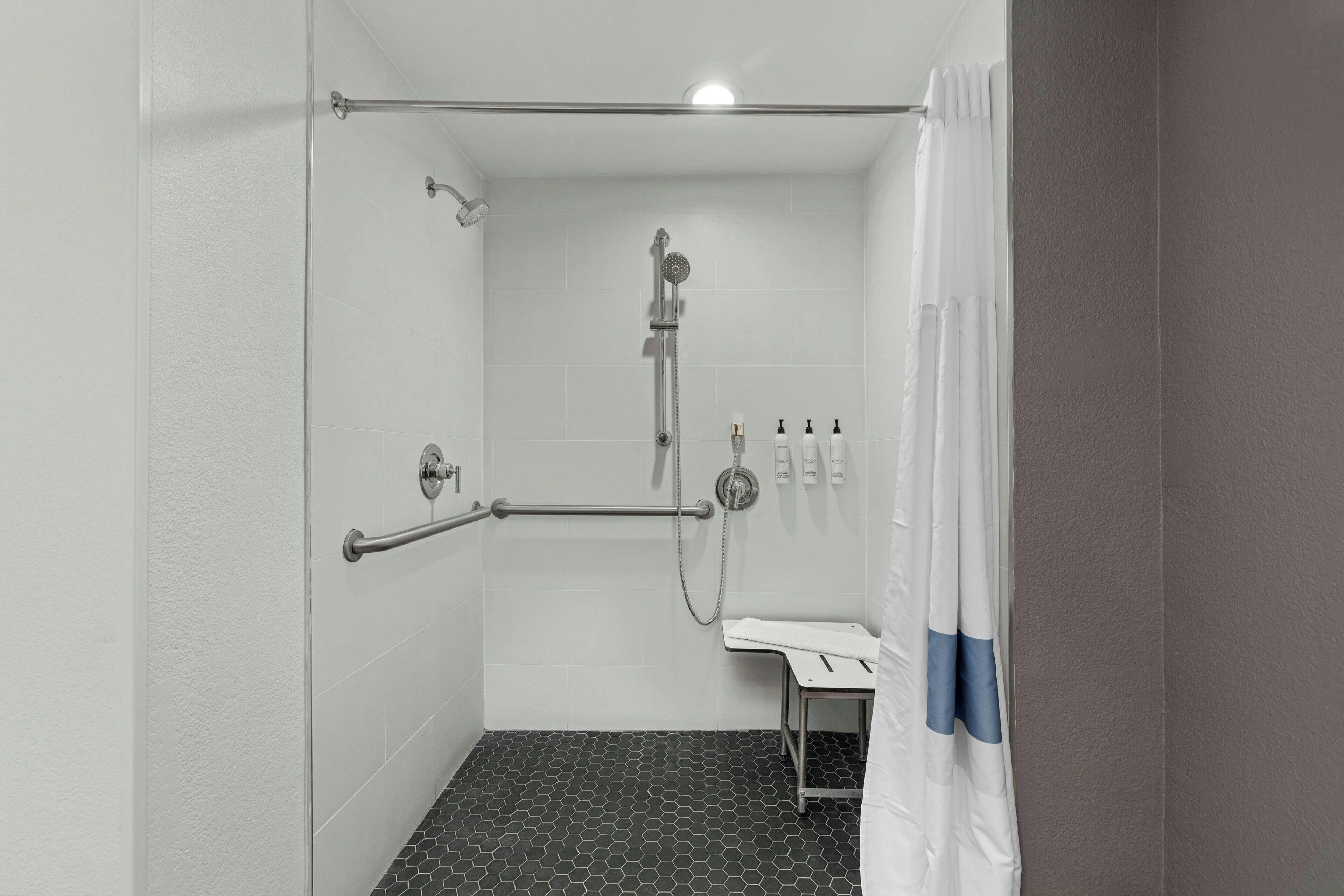A small, enclosed shower area with a grab bar, a handheld showerhead, and a white sink with a blue accent.