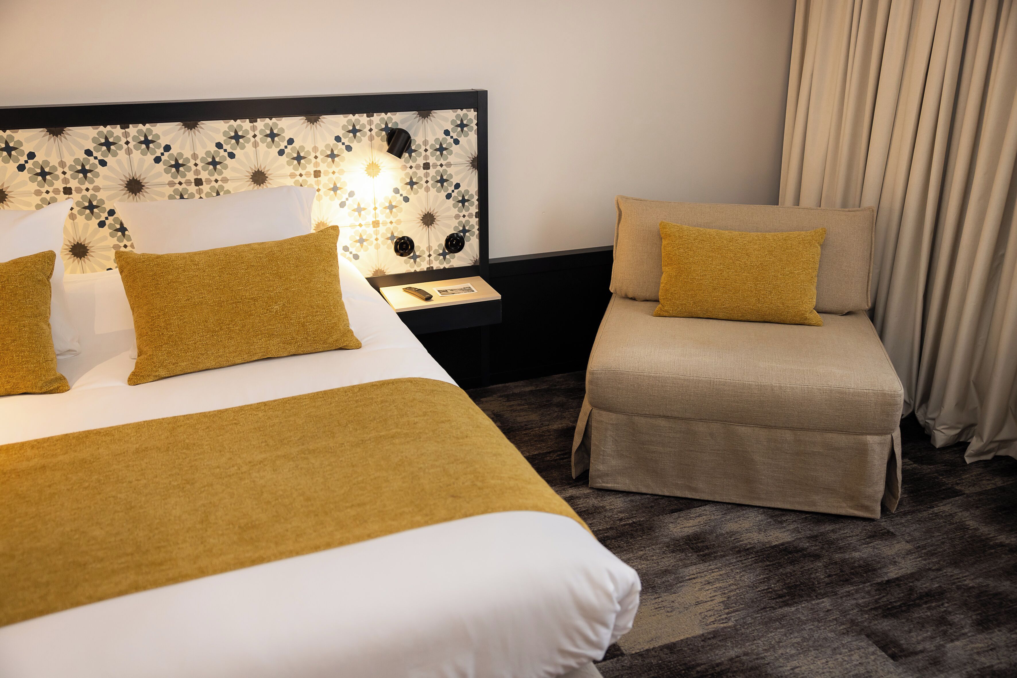 Una habitación de hotel con una cama, una mesita de noche, una silla y una cortina.
