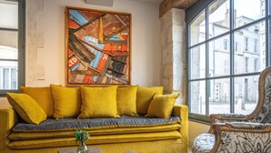 A room with a mustard-colored sofa, a patterned armchair, and a large abstract painting on the wall. - Hotel Saint Nicolas (La Rochelle)