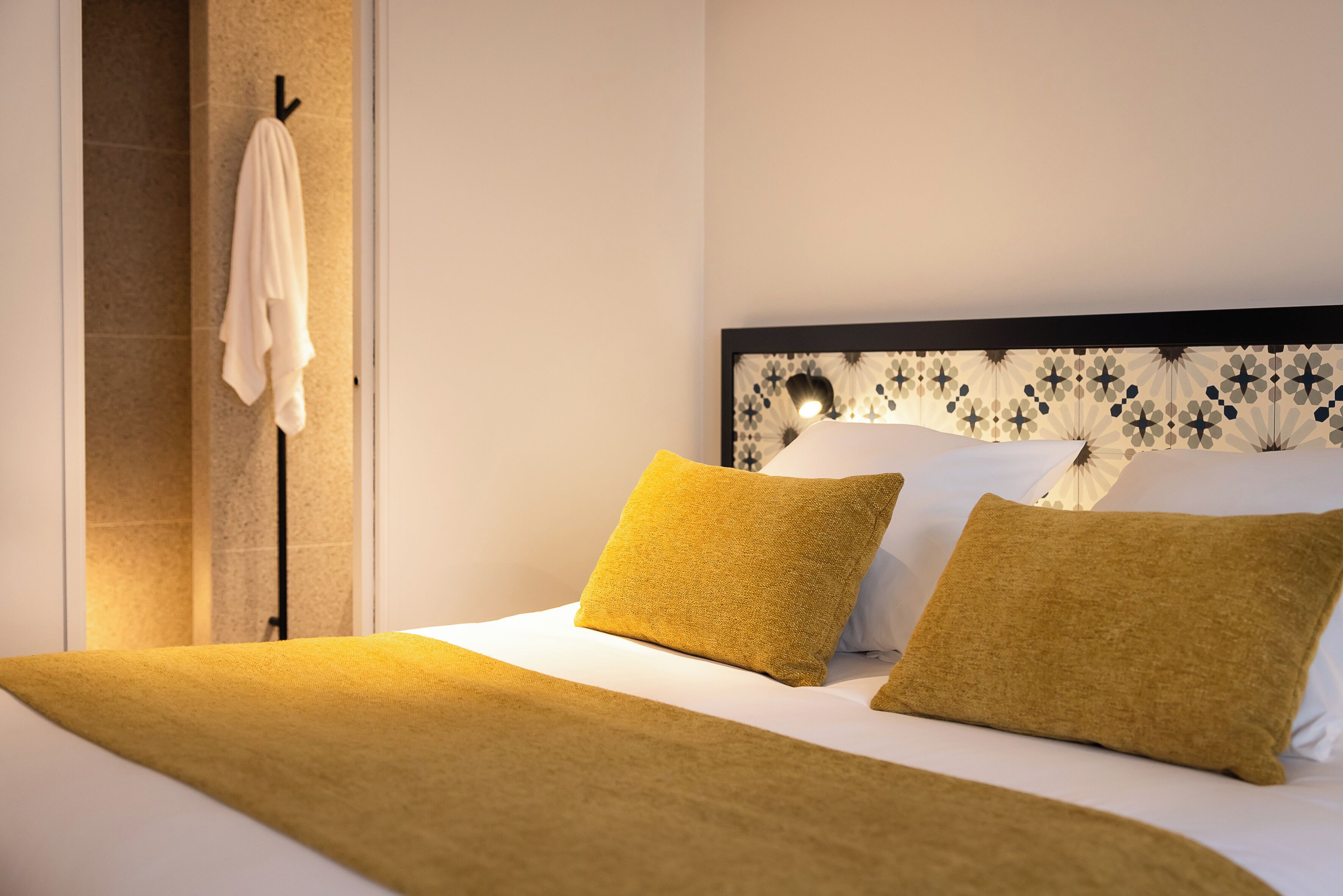 Un dormitorio con una cama, dos almohadas, una colcha y una pared con un diseño estampado.