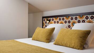 Una cama bien tendida con sábana blanca y dos almohadas color mostaza, cabecera estampada y pared lisa.