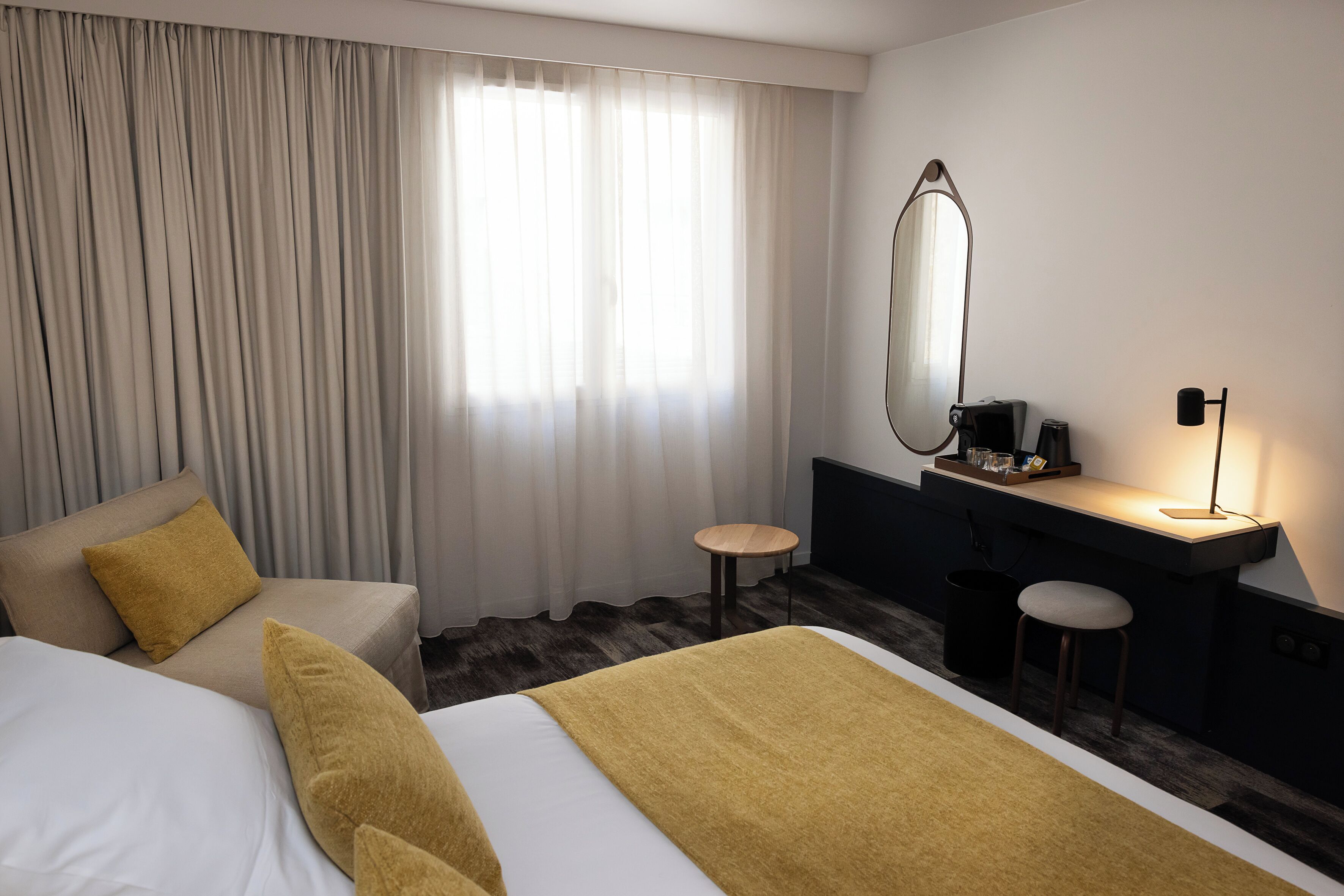 Ein Hotelzimmer mit zwei Betten, einem Schreibtisch, einem Stuhl, einem Spiegel und einer Lampe.