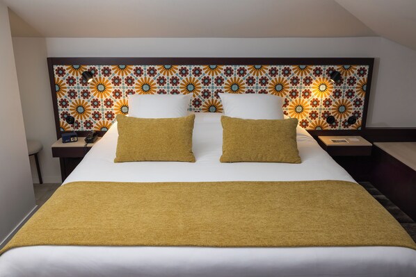A hotel room with a large bed, a headboard with a floral pattern, and a bedside table with a lamp.
