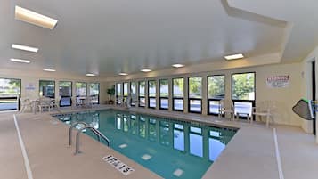 An indoor swimming pool with clear water, surrounded by windows and chairs.