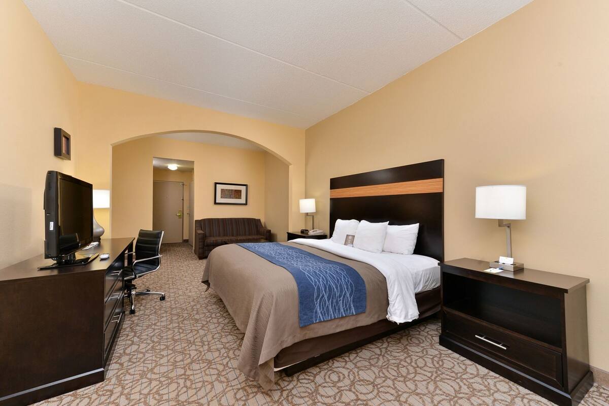 A hotel room with a bed, desk, TV, and a chair.