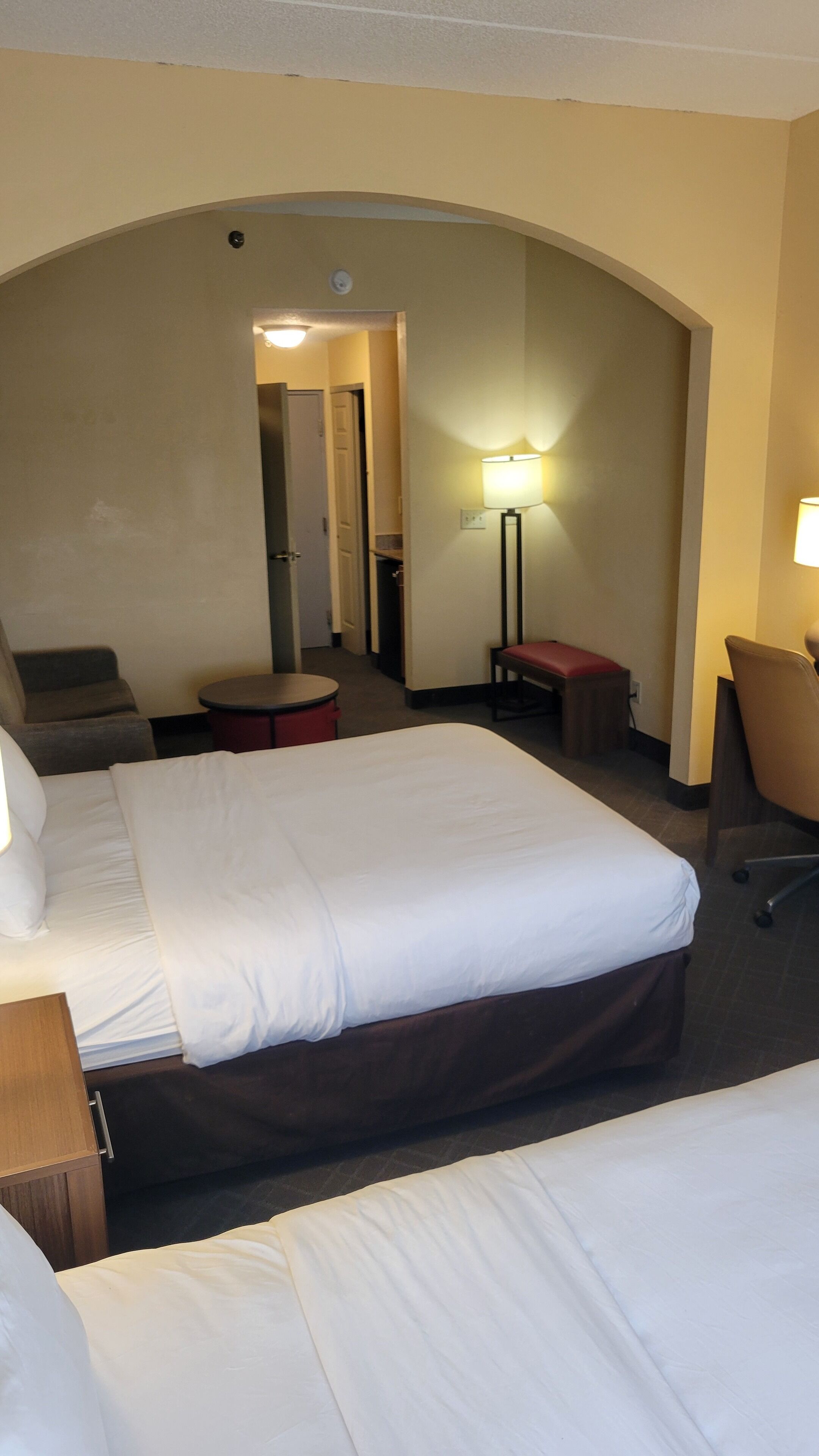 Una camera d'albergo con due letti, una scrivania, una sedia, una lampada e un tavolino.