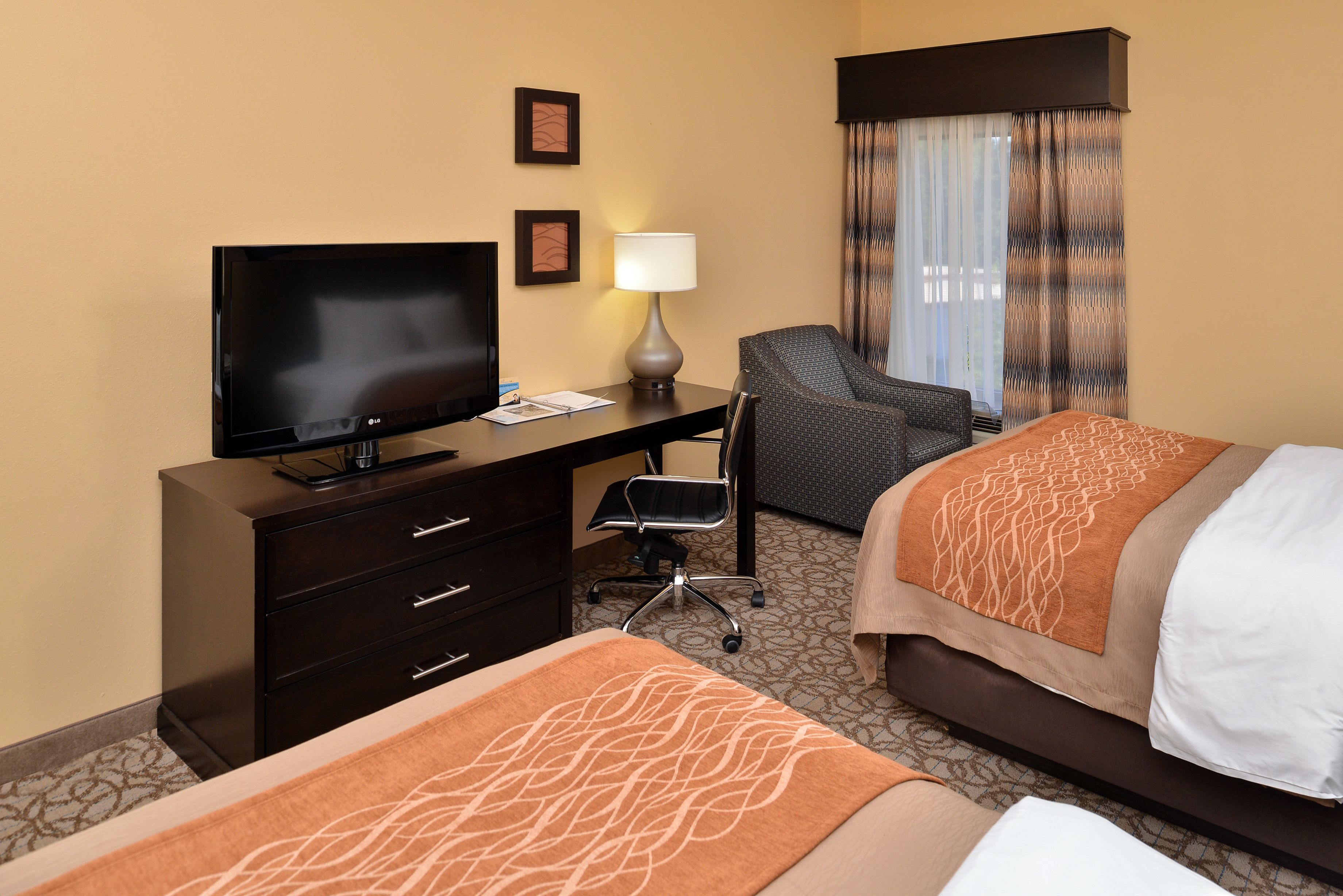 A hotel room with a bed, a desk with a TV, a chair, and a lamp.