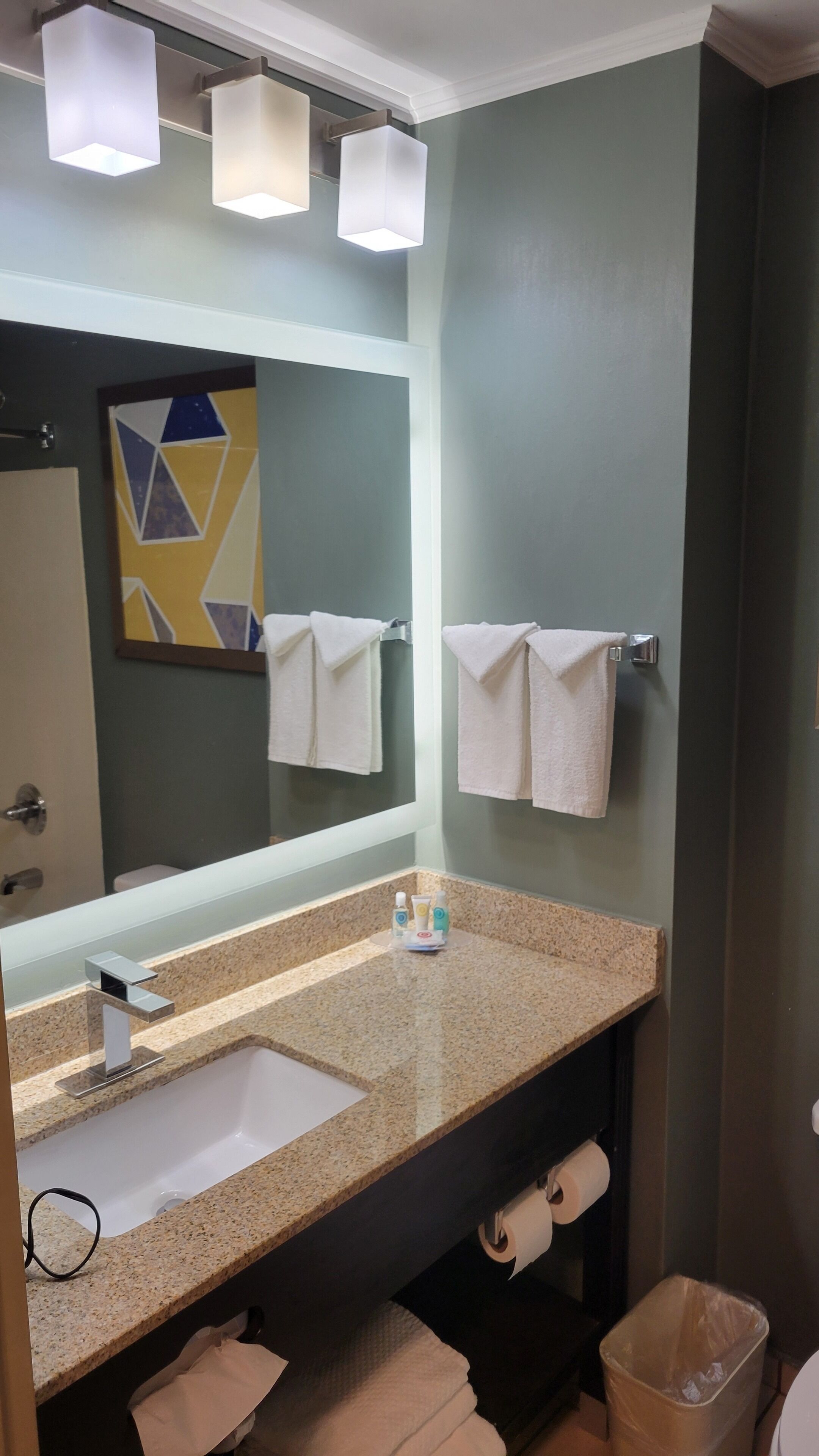 Une salle de bain avec un comptoir en granit, un lavabo, un miroir et deux serviettes suspendues à des porte-serviettes.