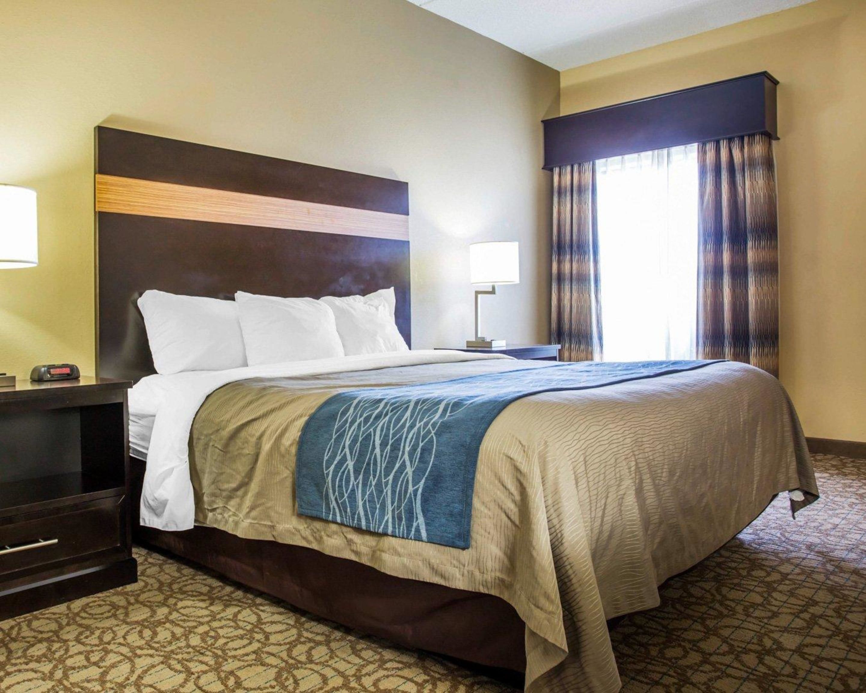 A hotel room with a large bed, a nightstand with a lamp, and a window with curtains.