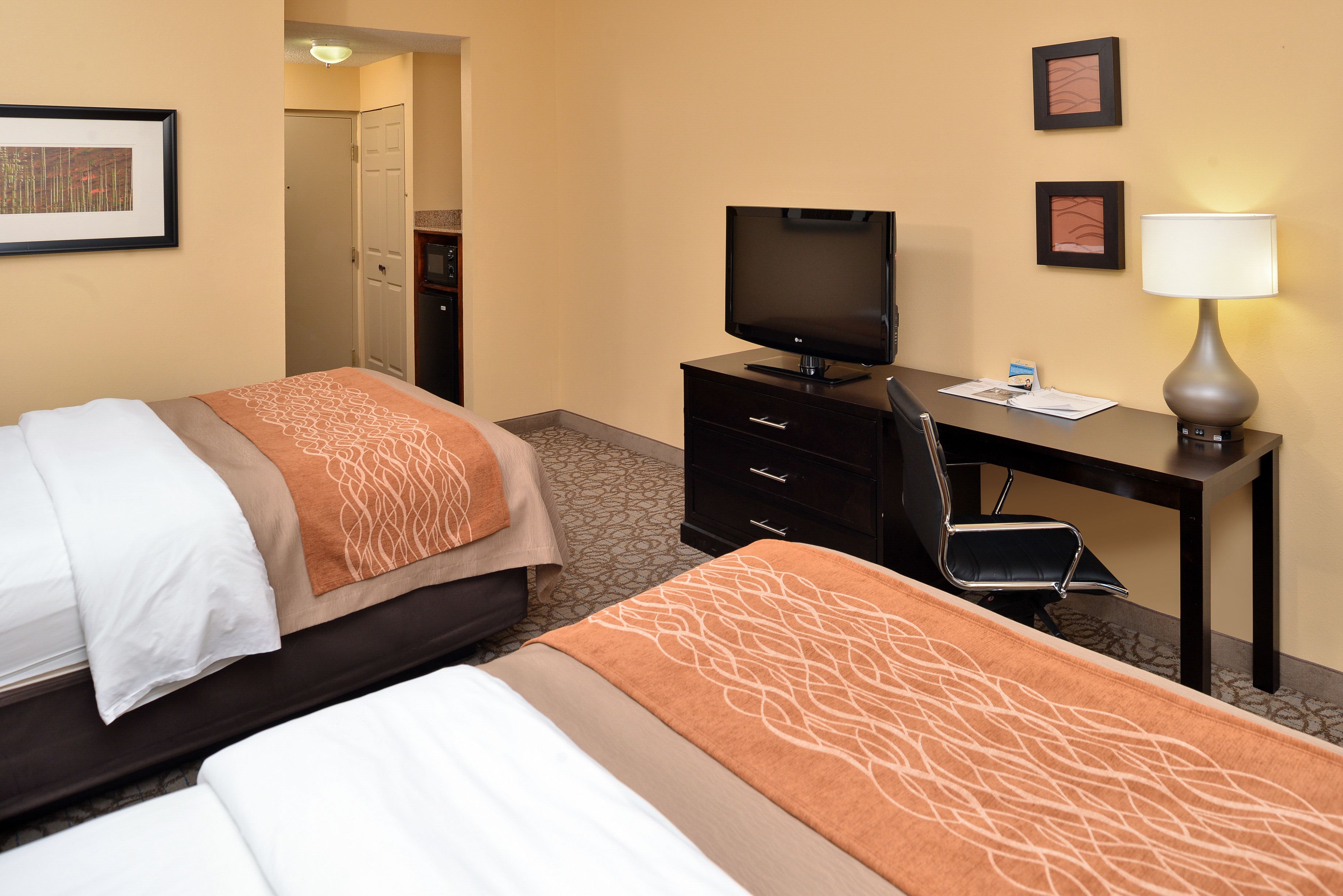 A hotel room with two beds, a desk with a television, a chair, and a lamp.