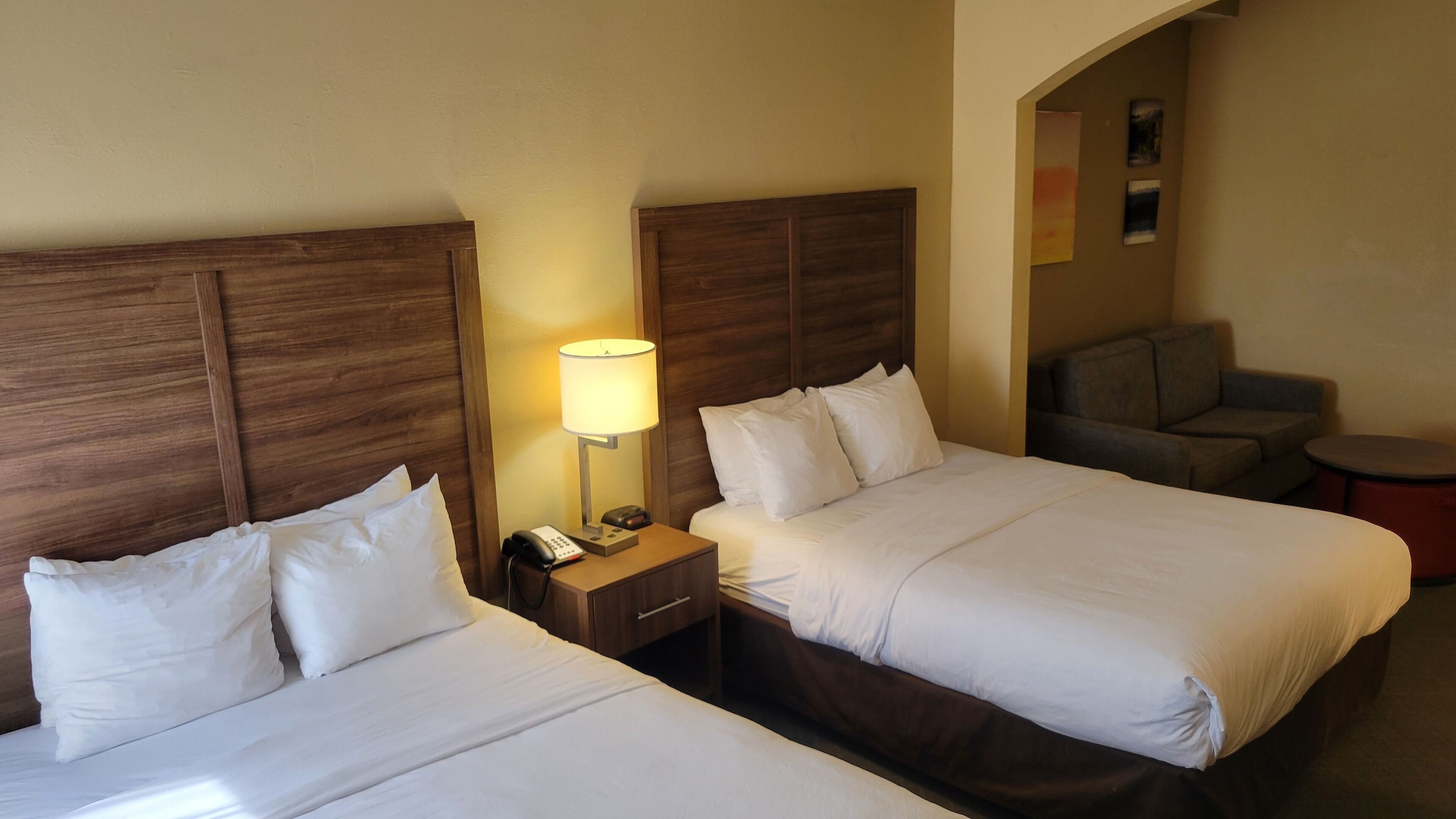 A hotel room with two beds, a nightstand with a lamp, a phone, and a small table.