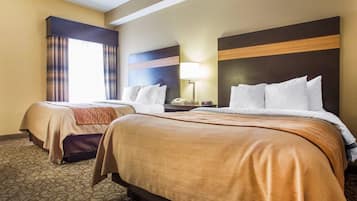 A hotel room with two beds, a nightstand, a lamp, and a window with curtains.